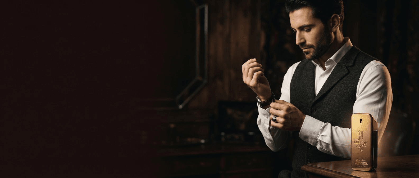 Hombre ajustándose el reloj en una habitación en penumbra, con un frasco de perfume sobre la cómoda